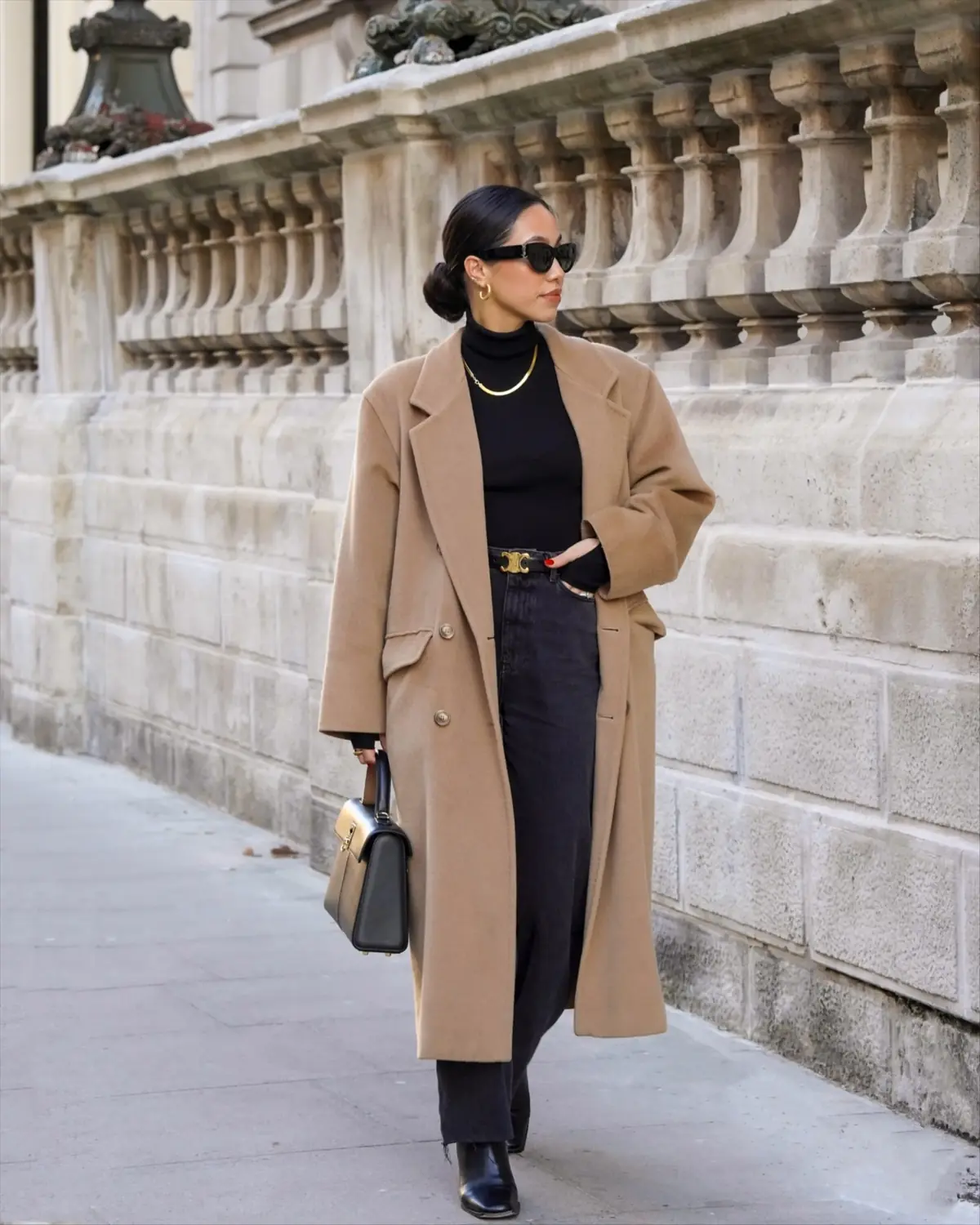 Woman wearing a camel coat with a black turtleneck and dark jeans for a modern cold weather outfit