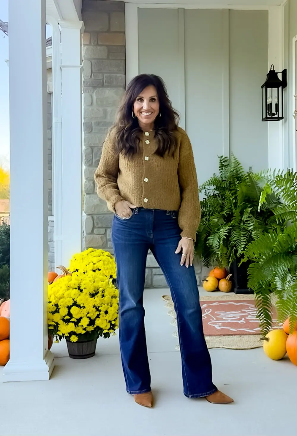 Woman wearing a caramel button cardigan with dark bootcut jeans on a fall porch