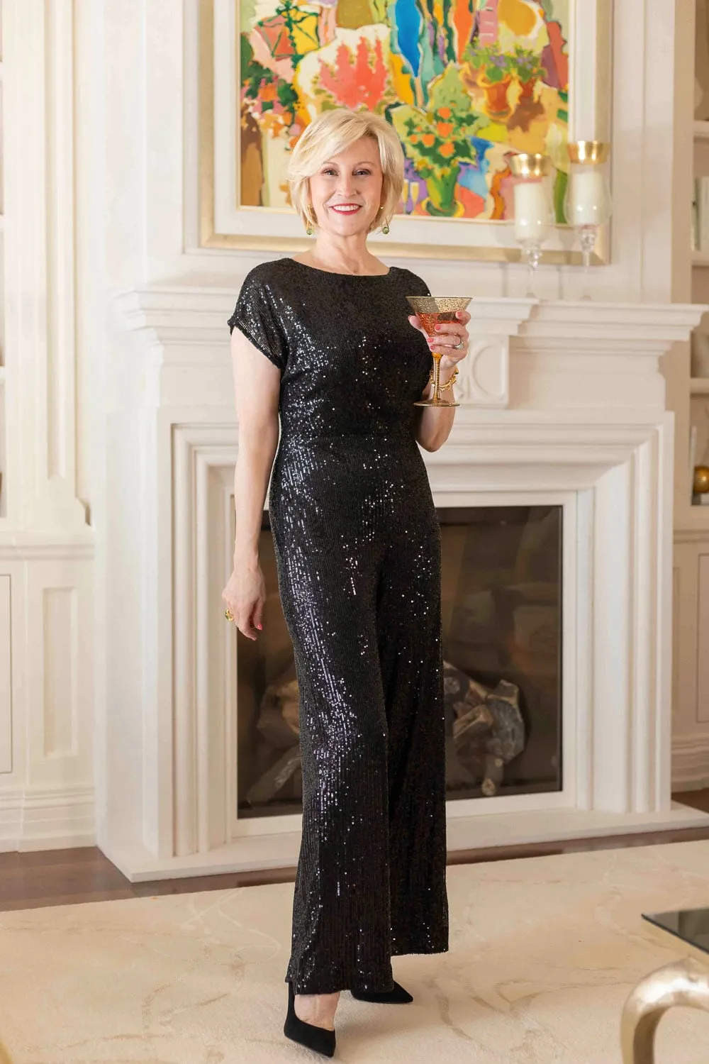 Woman over 40 wearing a black sequin wide leg jumpsuit for a company holiday party