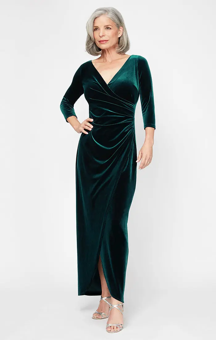 A silver haired woman wearing an emerald velvet floor length gown with three quarter sleeves and silver heels