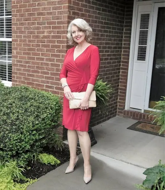 A silver haired woman wearing a red wrap dress with nude pumps and a neutral clutch for an elegant Christmas dinner