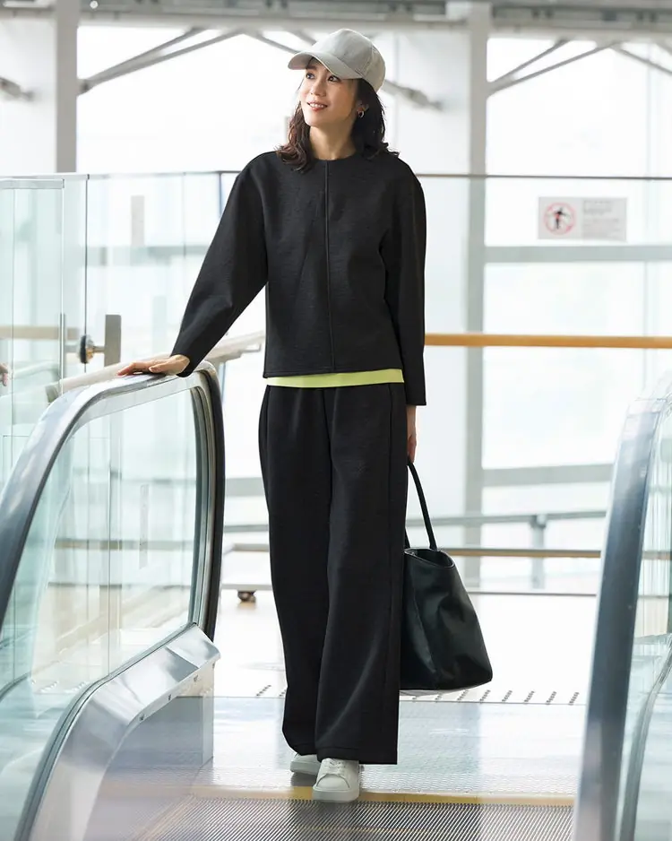 Mature woman wearing a black knit travel set with white sneakers and a tote at an airport