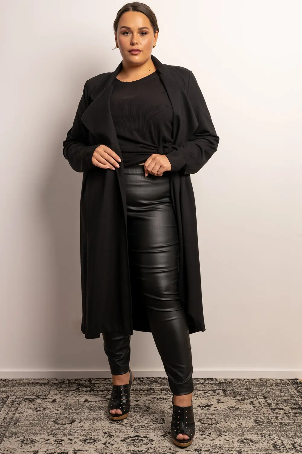 Plus size woman wearing faux leather pants with a black top and long coat for date night