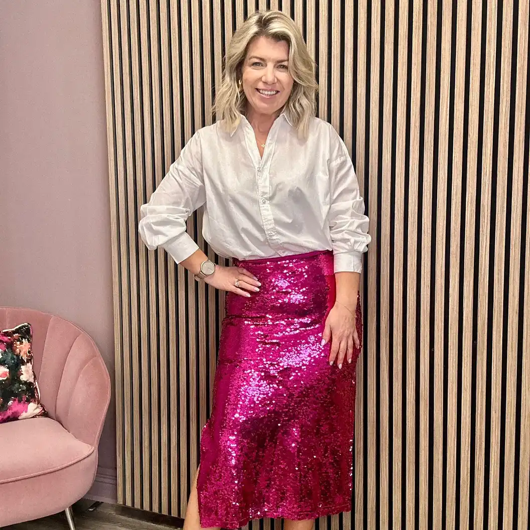 Woman wearing a white button down shirt with a fuchsia sequin midi skirt for an office party