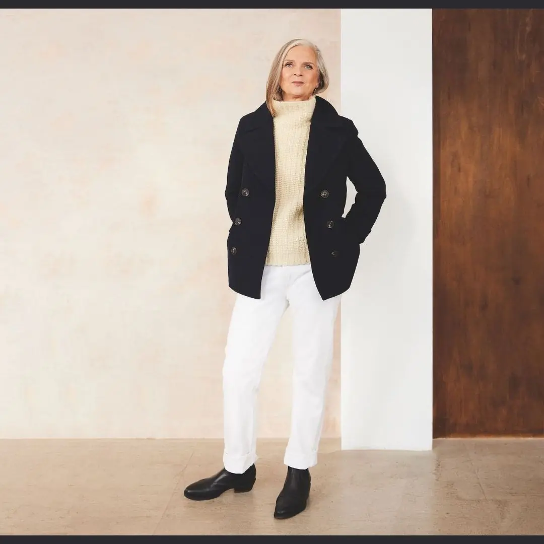 Woman over 50 styling a navy peacoat with white jeans and black ankle boots in winter