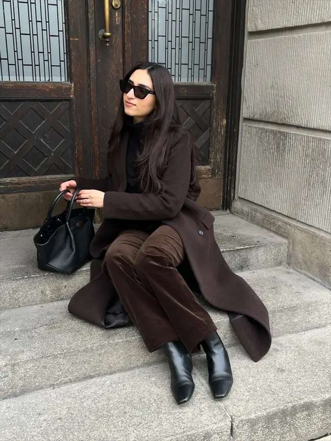 Woman wearing a chocolate brown coat with tonal trousers and black winter accessories