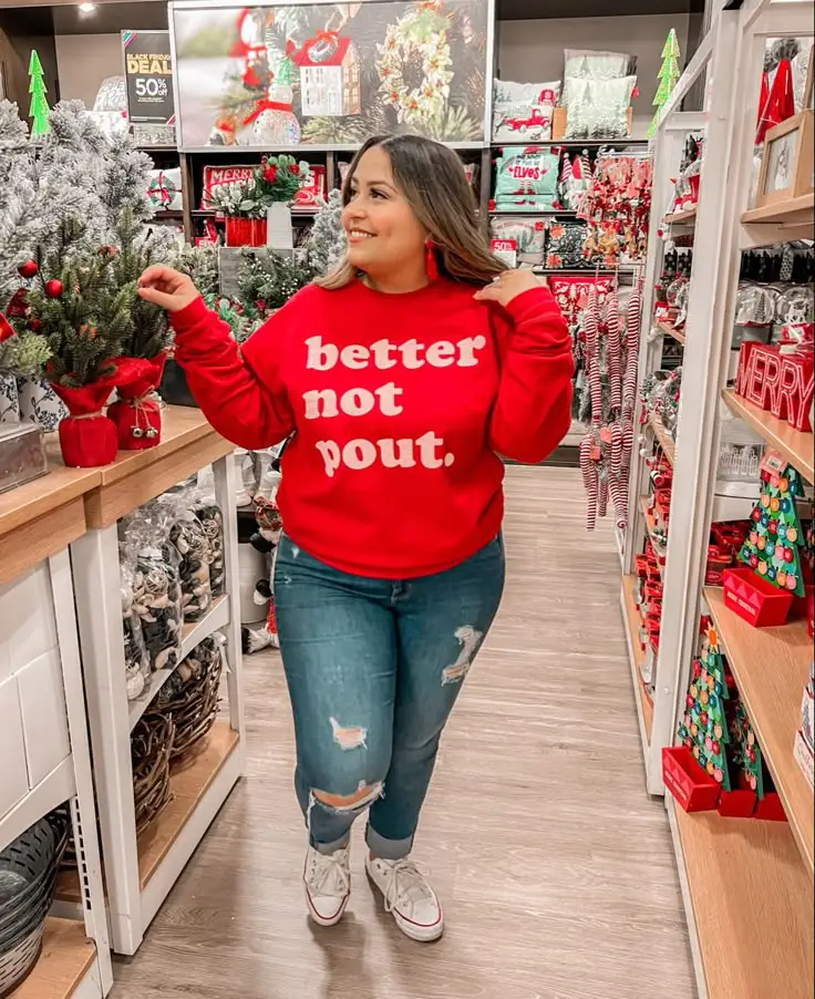 Midsize woman wearing a red Christmas slogan sweater with ripped jeans and white sneakers
