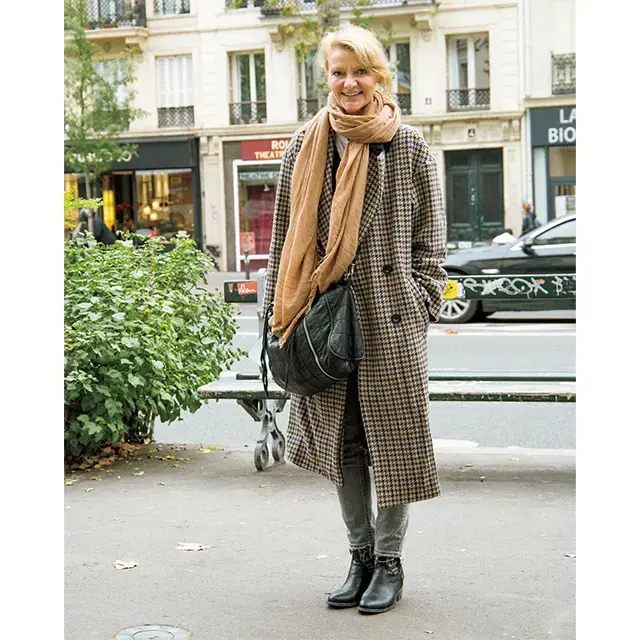 Woman wearing a houndstooth coat with grey jeans, camel scarf, and ankle boots for city travel