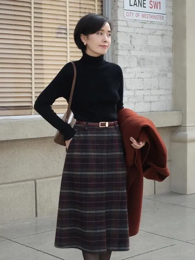 Woman wearing a plaid midi skirt with a fitted black turtleneck for winter church