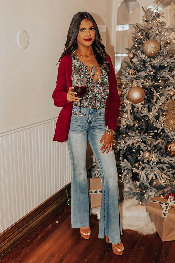 Woman wearing a wine cable knit cardigan floral blouse and light wash flared jeans at Christmas