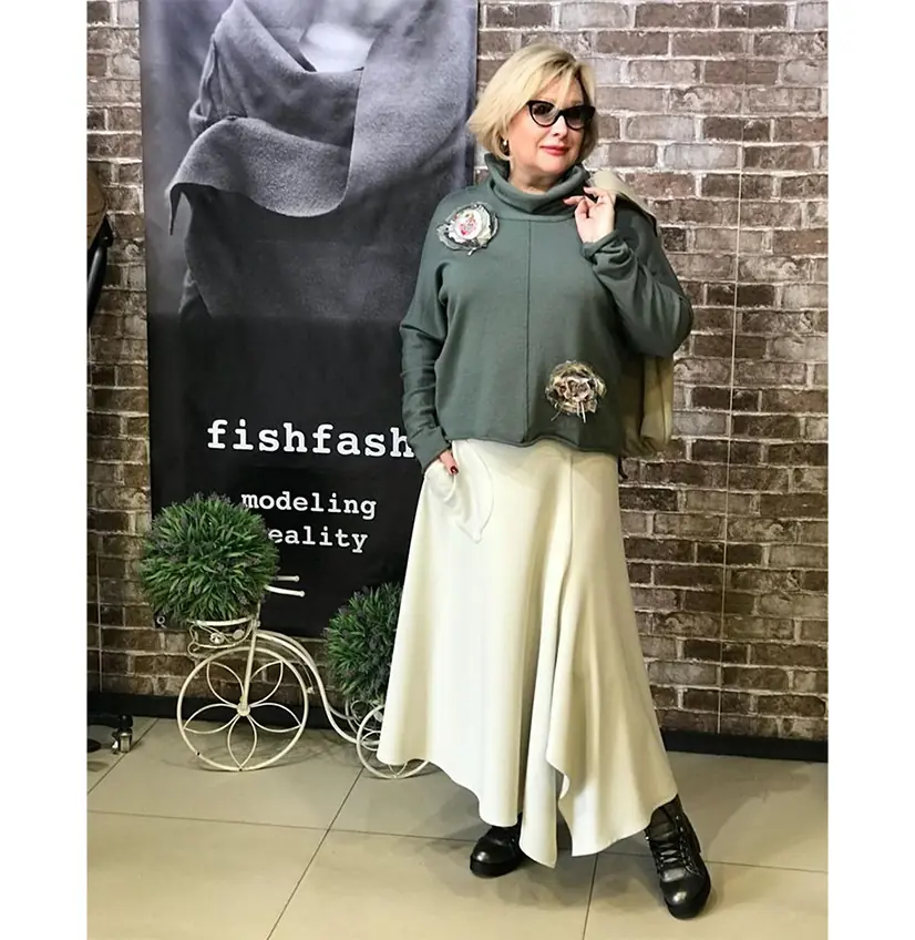 Mature woman wearing a sage sweater with a flowing cream skirt and black boots