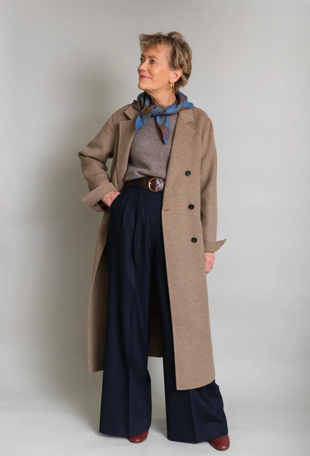 Woman over 50 wearing tailored wide leg trousers with an elegant belted winter coat