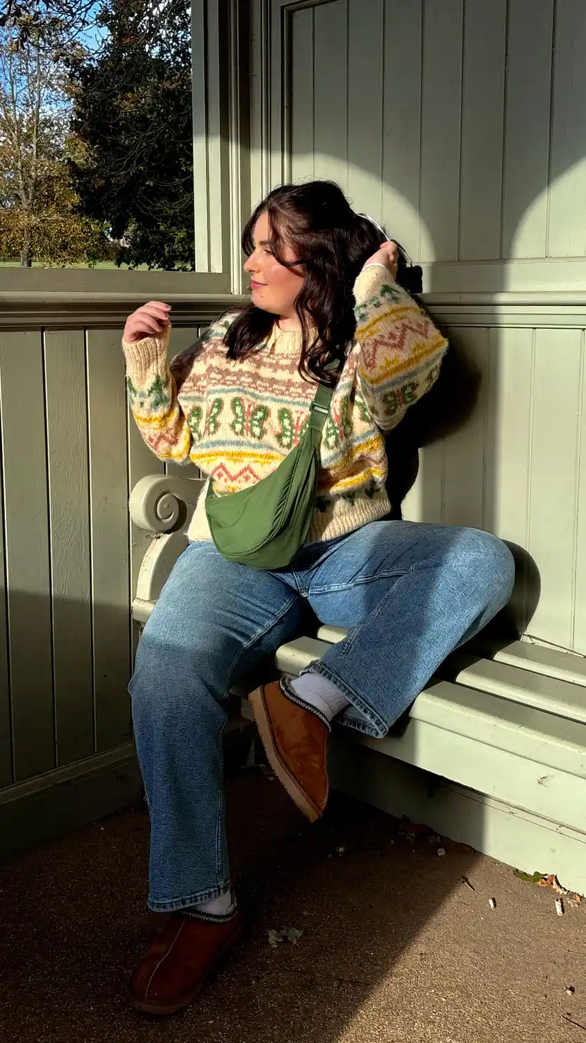 Curvy woman wearing a cream Fair Isle sweater with straight blue jeans and brown slip on shoes