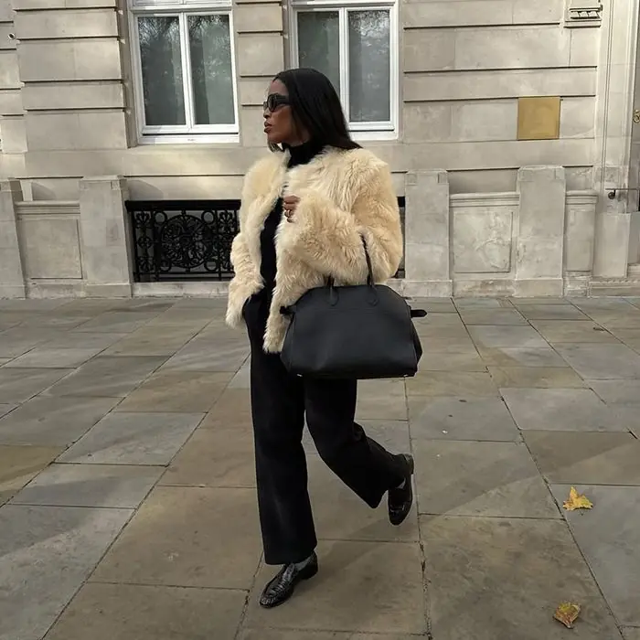 Woman wearing a cream faux fur jacket with black trousers and loafers for a chic winter look