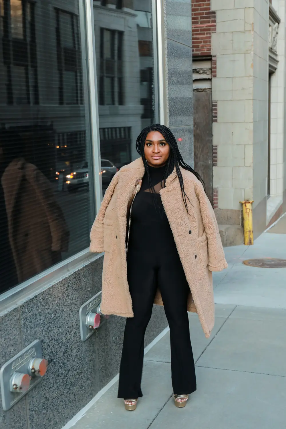Midsize woman wearing a black jumpsuit with a camel teddy coat for a winter dinner date
