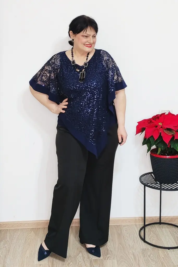A woman over 50 wearing a navy sequin and lace top with black wide leg trousers and navy pumps