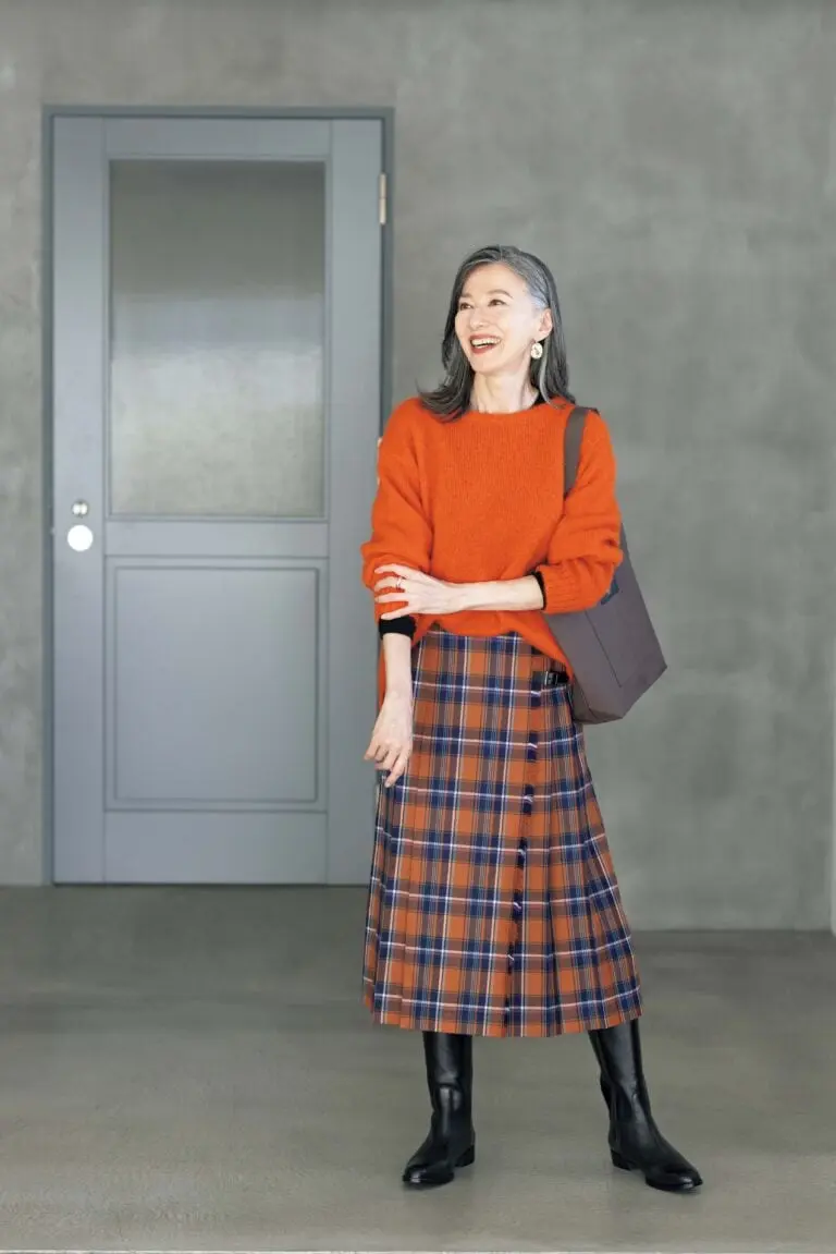 Woman in an orange sweater, plaid midi skirt and black knee high boots