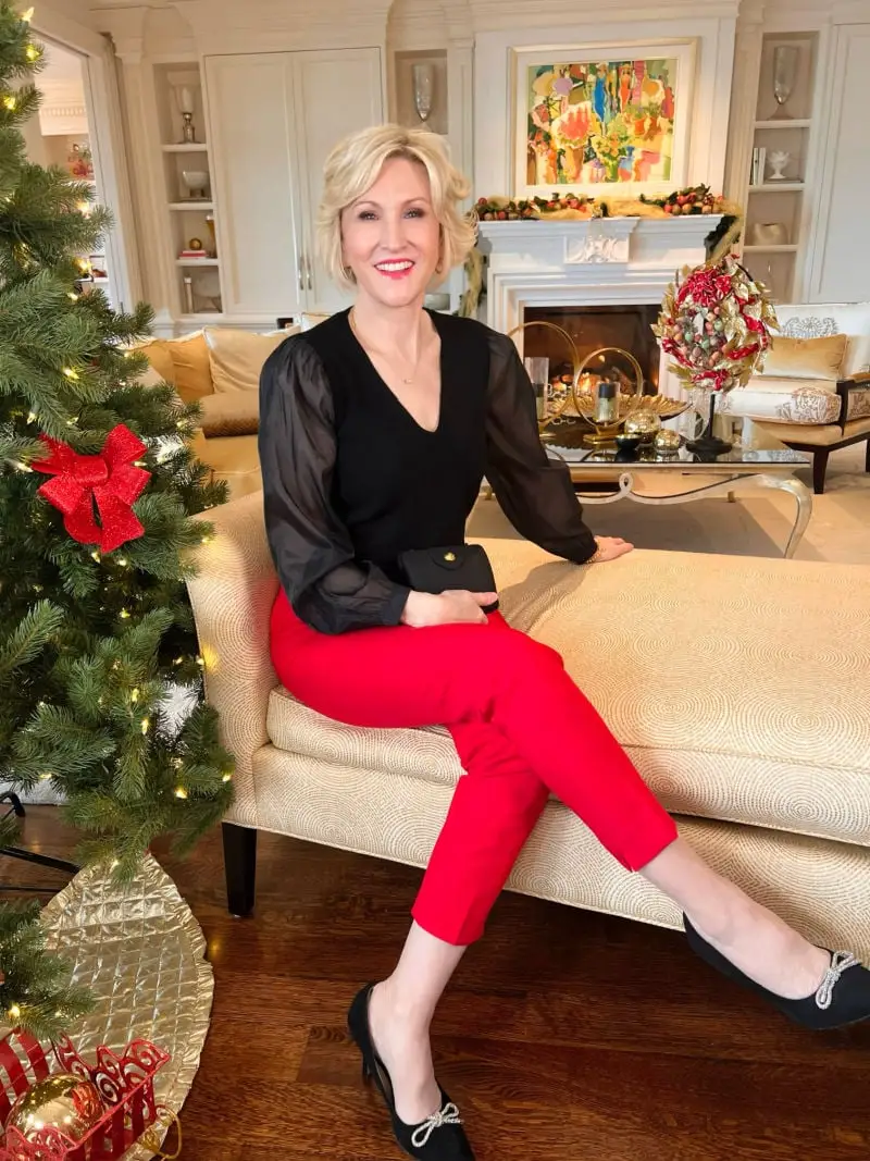 Woman over 40 wearing red tailored ankle pants with a black sheer sleeve top