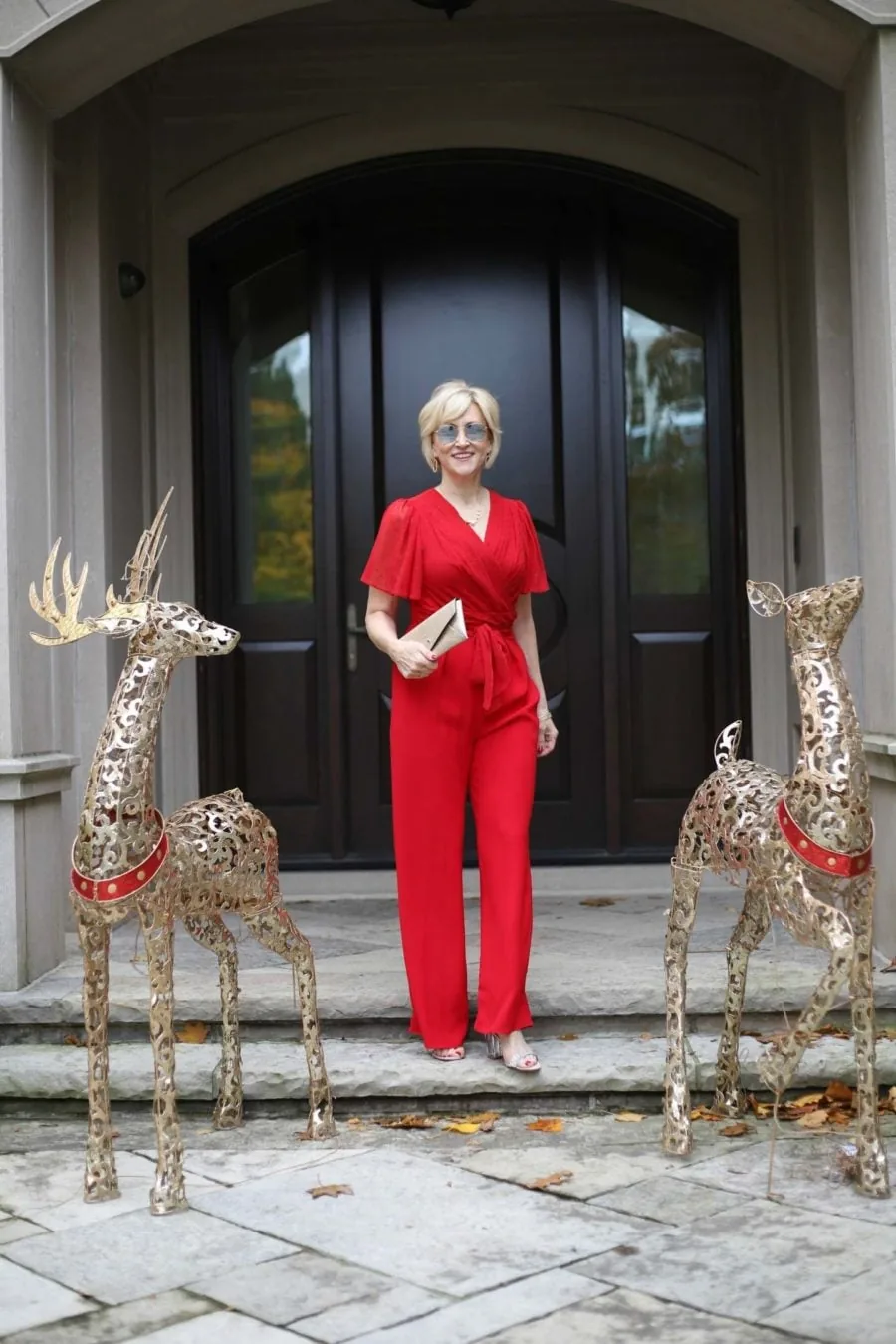 Woman over 50 wearing a red wide leg jumpsuit with a gold clutch for a holiday party