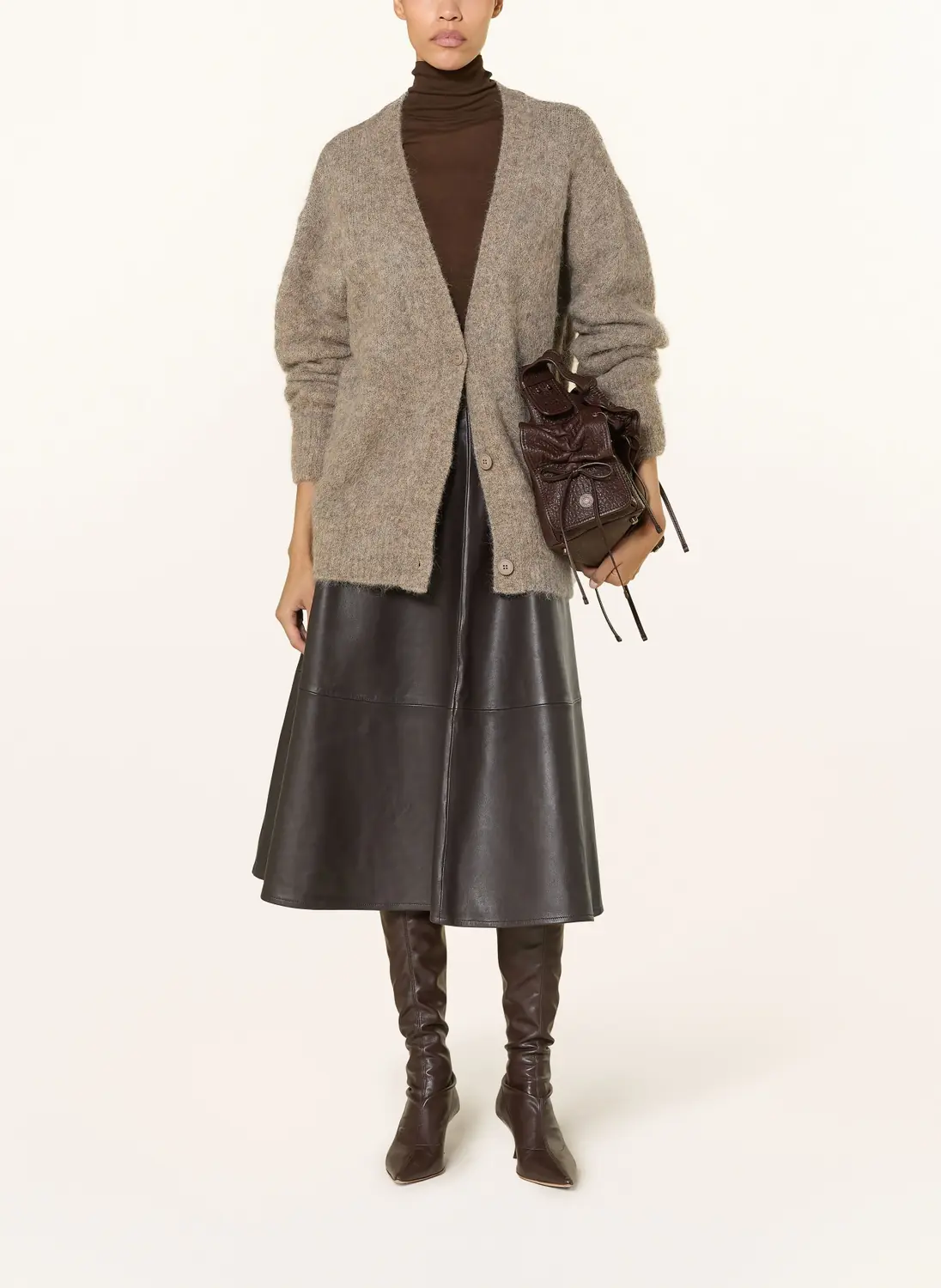 Woman over 50 styling a chunky cardigan with a midi skirt and tall boots