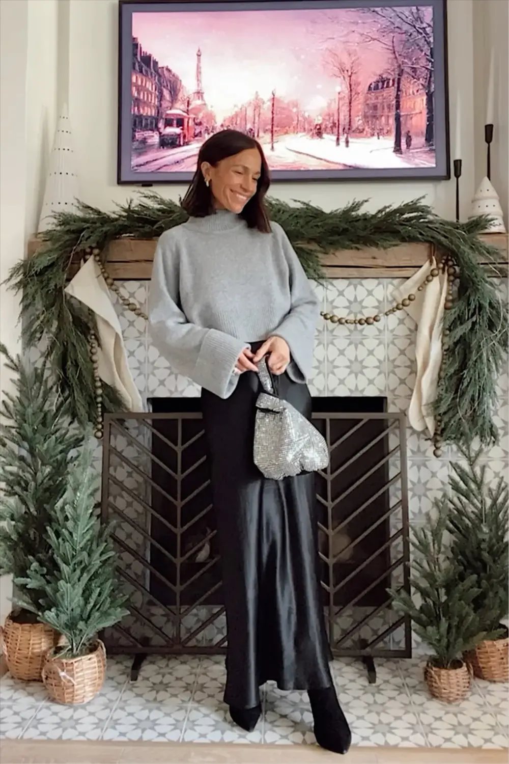 Woman over 50 in a gray cashmere sweater and black satin maxi skirt for an understated New Year’s Eve look