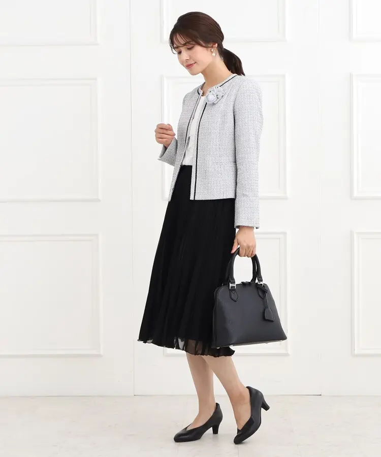 Woman wearing a light tweed jacket with a black pleated midi skirt and pumps for church