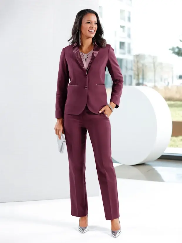 A woman wearing a burgundy tailored pantsuit with satin lapels, metallic heels and a silver clutch for a winter wedding