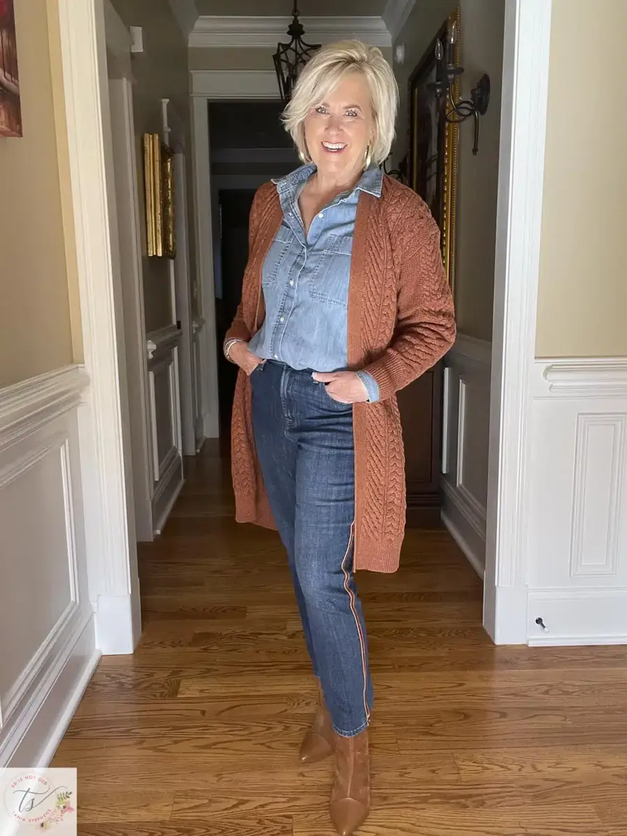 Woman in a denim shirt, rust cardigan and dark jeans