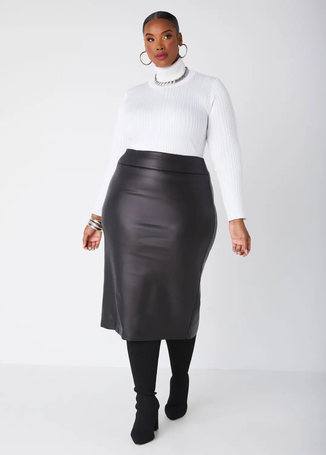 Plus size woman wearing a cream turtleneck with a black faux leather midi skirt and boots