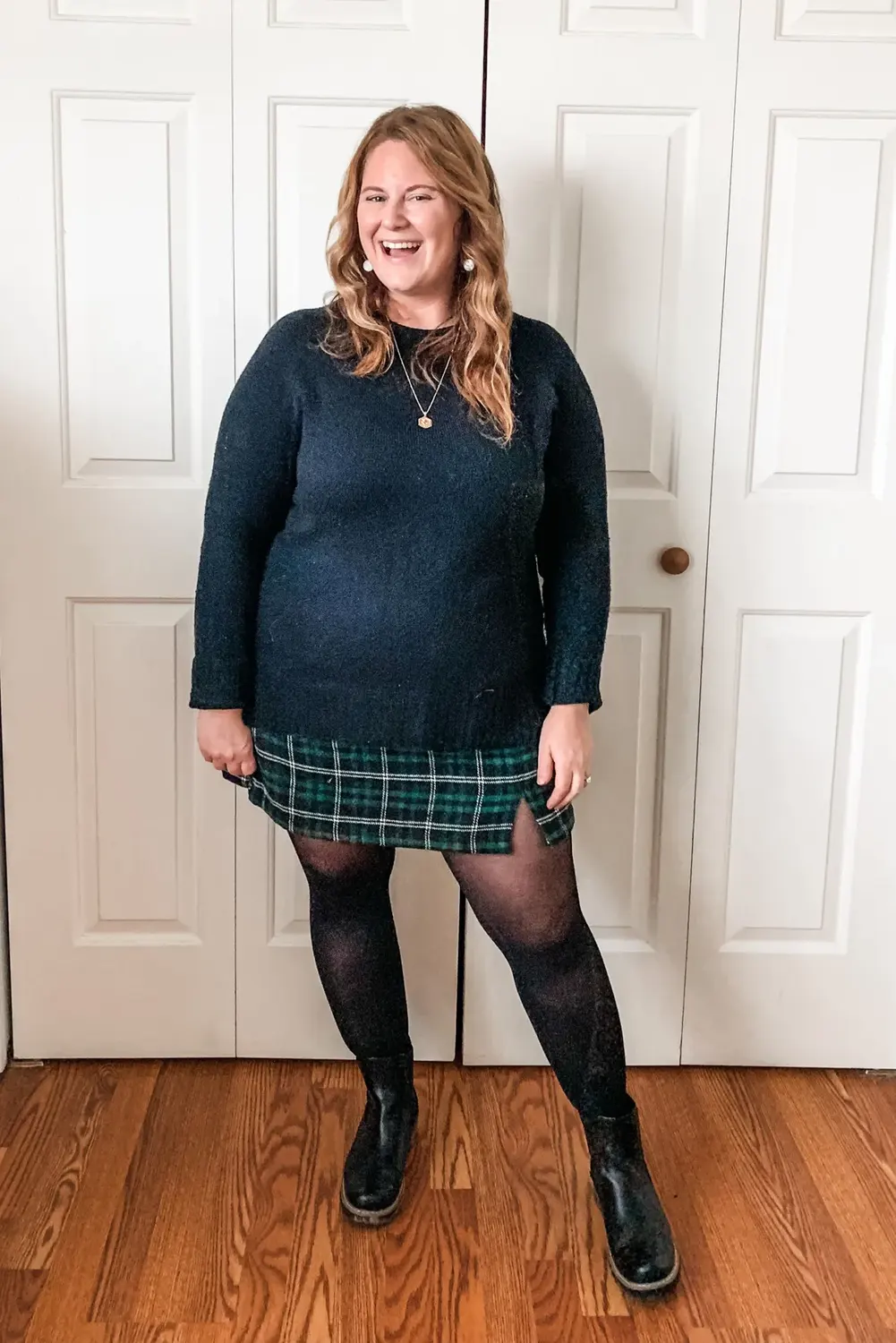 Midsize woman wearing a navy sweater with a green plaid skirt black tights and ankle boots