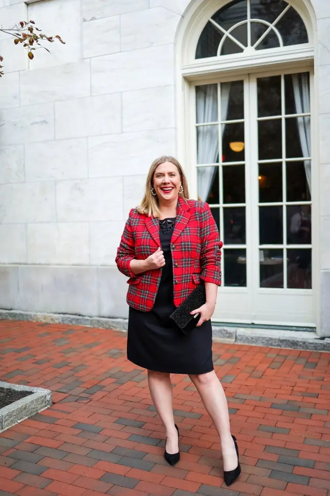A woman wearing a red plaid blazer over a black knee length dress with black pumps for Christmas dinner