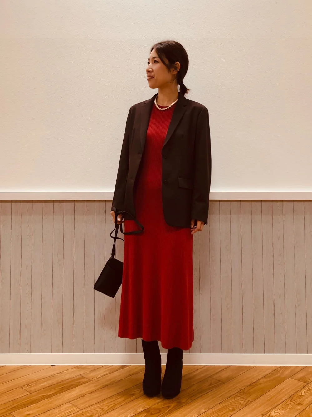 Woman wearing a red knit midi dress with a tailored black blazer pearls and ankle boots