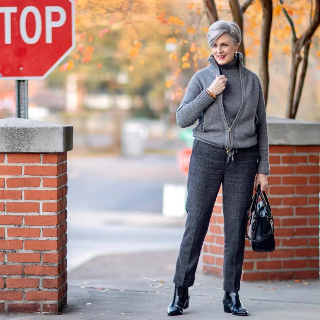 Woman over 50 wearing monochrome grey knit layers with plaid tailored trousers and boots