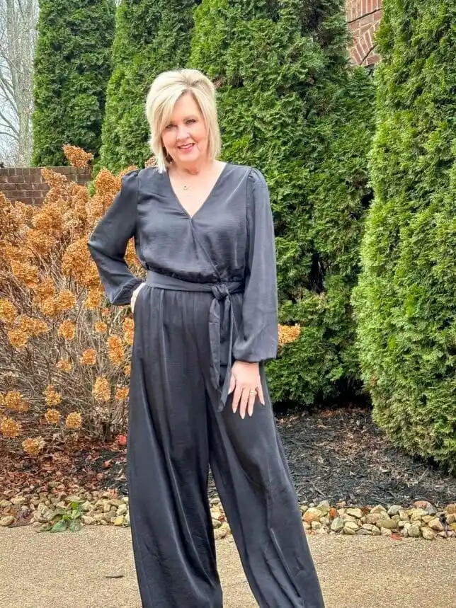 Woman over 50 wearing a black wrap jumpsuit with statement earrings for New Year’s Eve