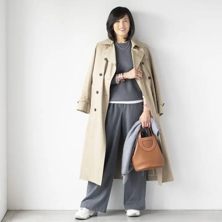 Woman in her 50s wearing grey knit layers with a beige trench and white sneakers for travel