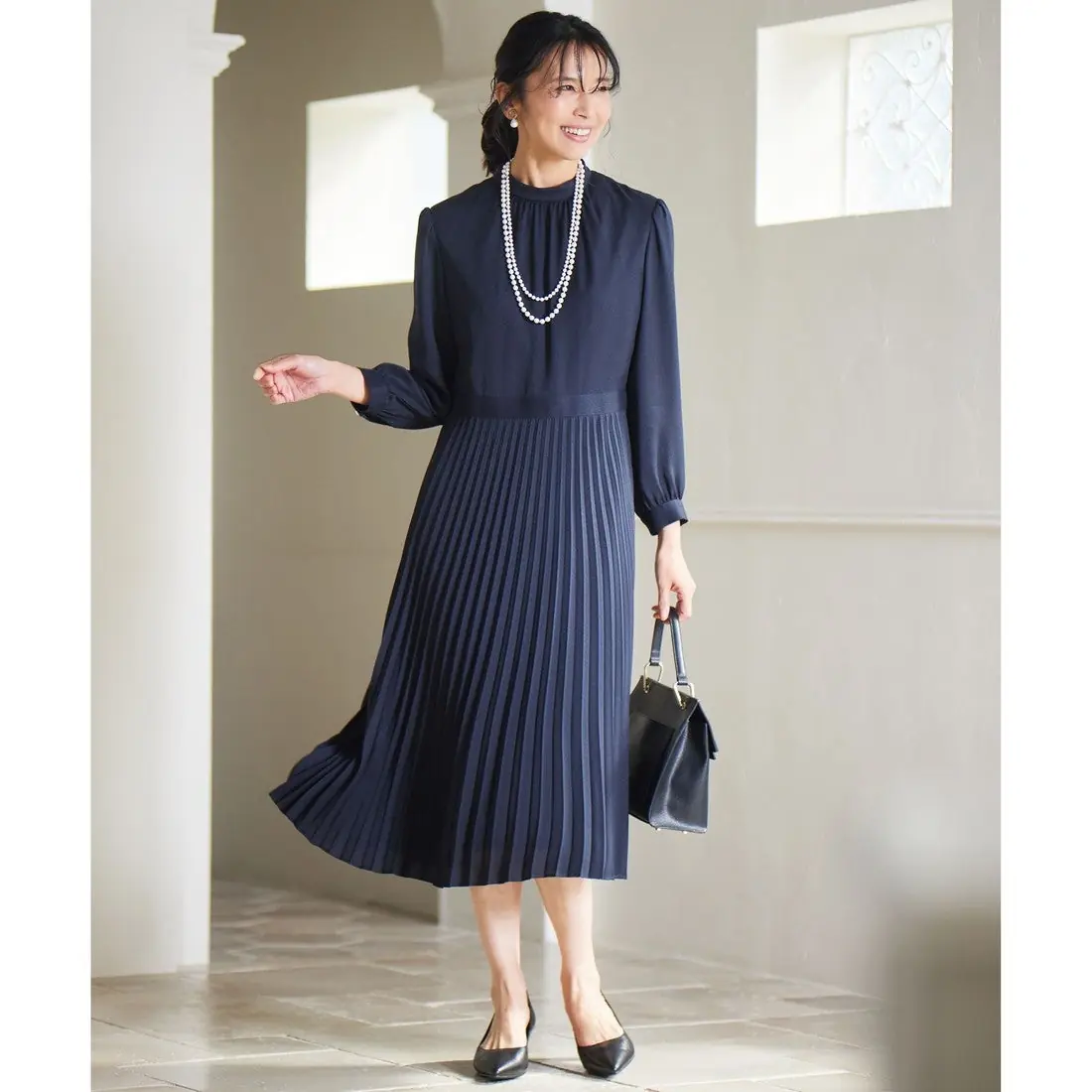 Woman wearing a navy pleated midi dress with long sleeves and black flats for church