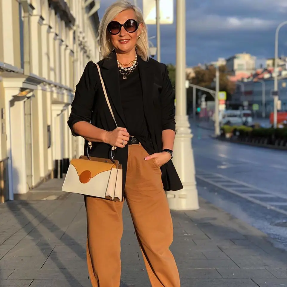Woman in a black blazer and camel wide leg trousers with a two tone bag