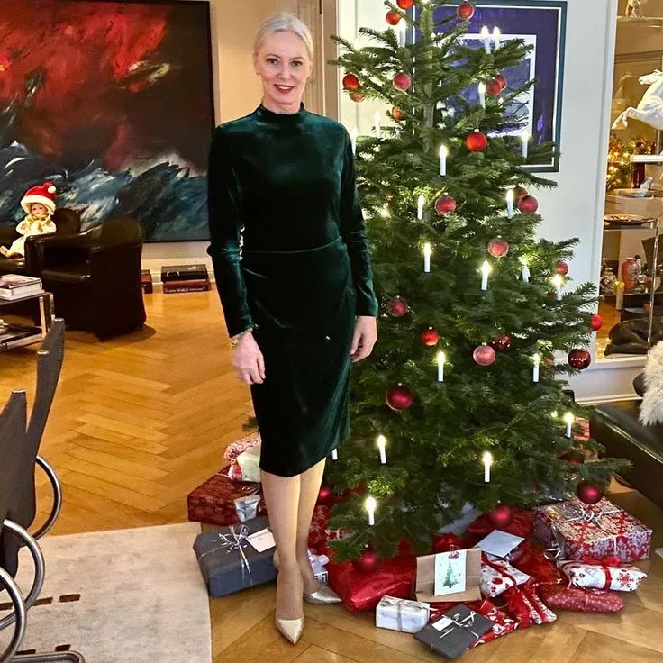 Mature woman wearing a dark green velvet midi dress beside a Christmas tree