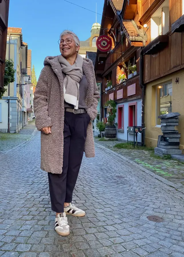 Woman in a brown teddy coat with dark trousers and white sneakers for a casual winter outfit