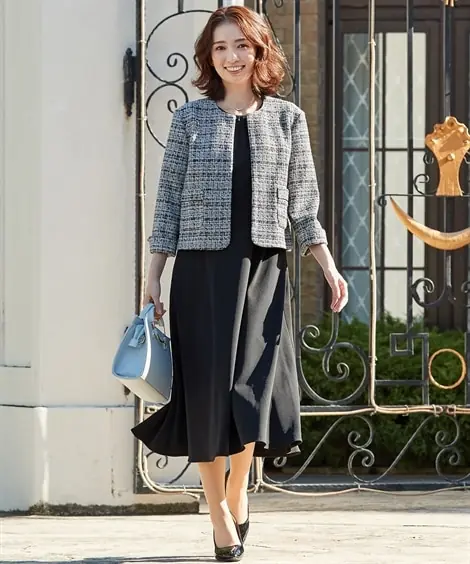 Older woman wearing a grey tweed jacket over a black knee length dress with pumps