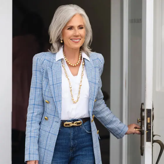 Woman in a light blue plaid blazer, white blouse and dark jeans with pearls