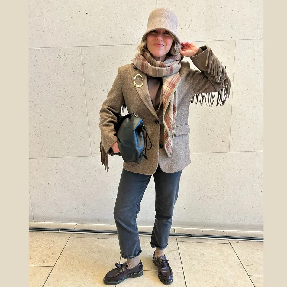Mature woman wearing a brown wool blazer with black jeans, scarf, hat, and loafers for travel