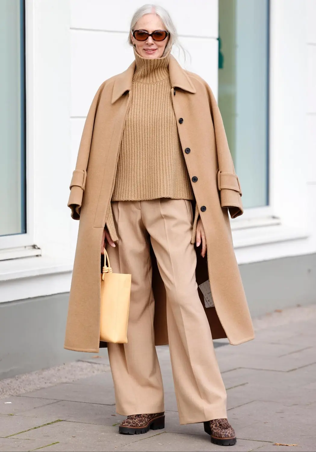 Mature woman wearing a long neutral wool coat over a matching winter knit set
